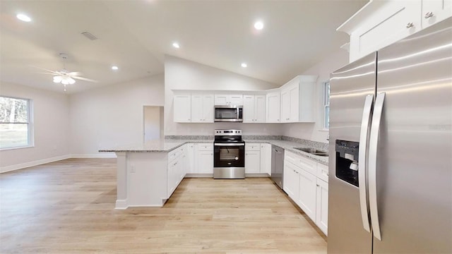 kitchen featuring light stone countertops, white cabinetry, stainless steel appliances, light hardwood / wood-style floors, and vaulted ceiling