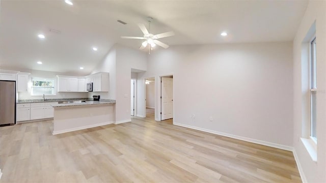 kitchen with light wood-type flooring, appliances with stainless steel finishes, kitchen peninsula, light stone countertops, and white cabinets