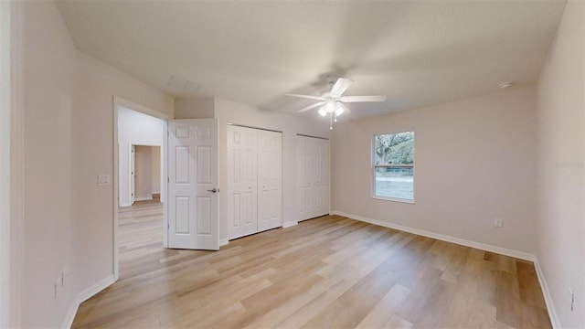 unfurnished bedroom featuring ceiling fan, light hardwood / wood-style floors, and two closets