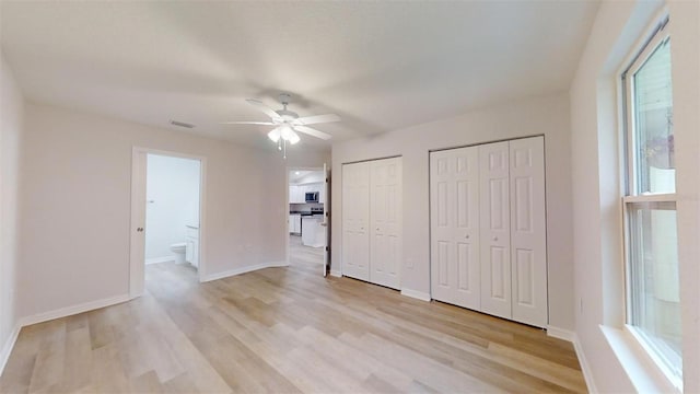 unfurnished bedroom featuring ceiling fan, connected bathroom, light hardwood / wood-style floors, and two closets