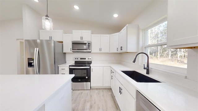 kitchen with hanging light fixtures, sink, white cabinets, lofted ceiling, and stainless steel appliances