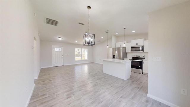 kitchen with a center island, appliances with stainless steel finishes, hanging light fixtures, white cabinets, and lofted ceiling