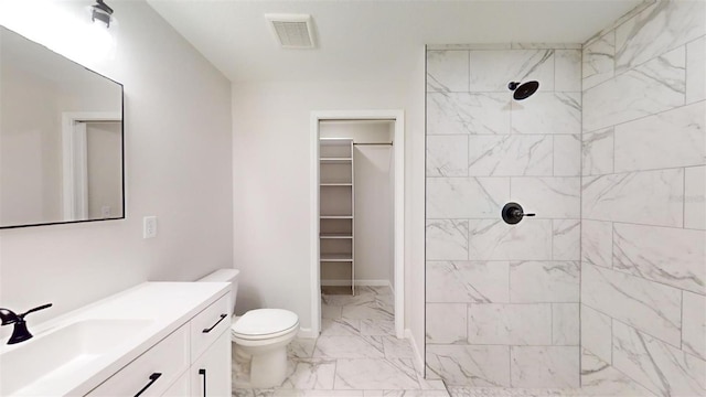 bathroom with a tile shower, toilet, and vanity