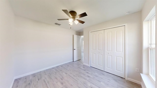 unfurnished bedroom with light wood-type flooring, a closet, multiple windows, and ceiling fan