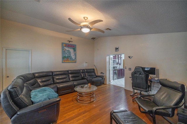 living room with a textured ceiling, ceiling fan, vaulted ceiling, and light wood-type flooring