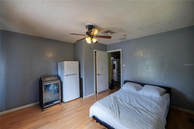 bedroom with ceiling fan, light hardwood / wood-style flooring, white fridge, and a textured ceiling