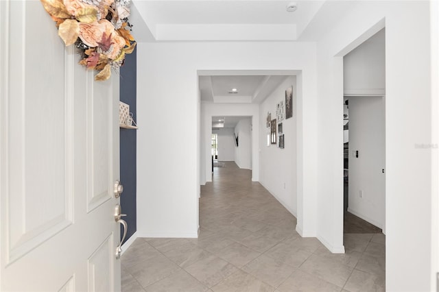 hall with light tile patterned floors and a raised ceiling