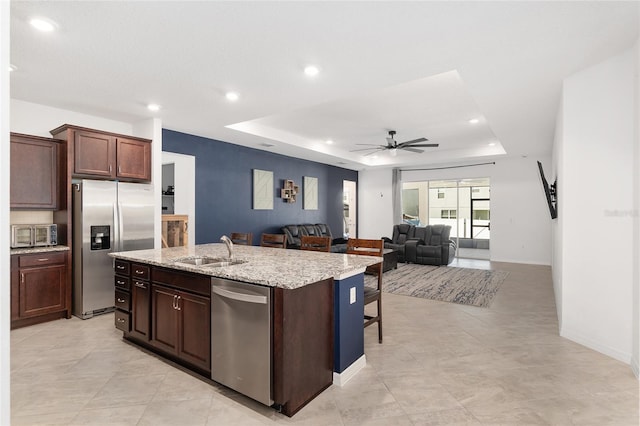 kitchen with a center island with sink, ceiling fan, appliances with stainless steel finishes, a raised ceiling, and sink