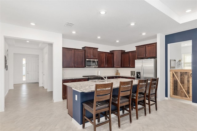 kitchen featuring a breakfast bar, sink, light stone counters, appliances with stainless steel finishes, and a kitchen island with sink