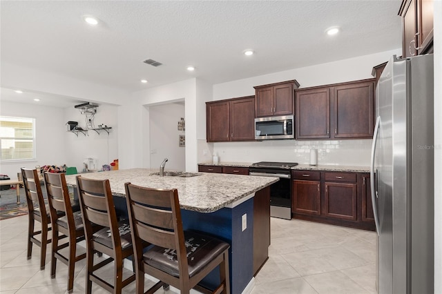 kitchen with stainless steel appliances, an island with sink, sink, light stone counters, and a breakfast bar area