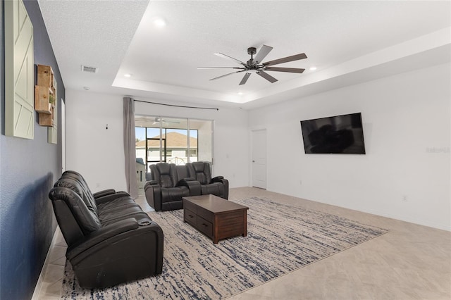 living room featuring ceiling fan, a raised ceiling, and a textured ceiling