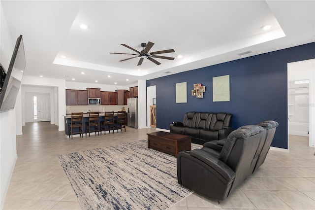 living room featuring ceiling fan, light tile patterned floors, and a tray ceiling