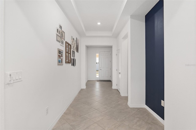 hallway with light tile patterned floors and a tray ceiling