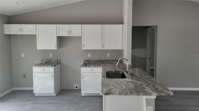 kitchen featuring vaulted ceiling, stone counters, kitchen peninsula, sink, and white cabinets