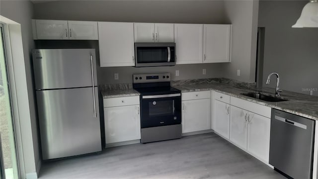 kitchen with white cabinets, light wood-style flooring, appliances with stainless steel finishes, light stone countertops, and a sink