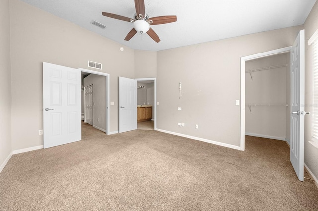 unfurnished bedroom featuring ceiling fan, a walk in closet, light carpet, and a closet