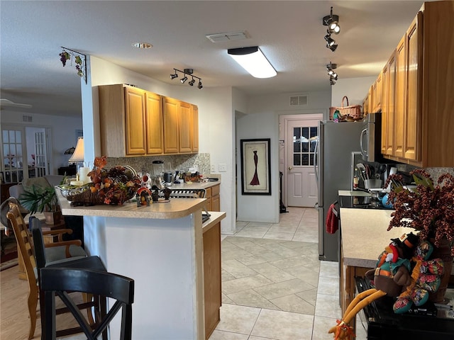 kitchen featuring kitchen peninsula, decorative backsplash, rail lighting, a breakfast bar area, and light tile patterned flooring