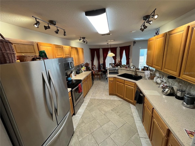 kitchen with sink, tasteful backsplash, a textured ceiling, decorative light fixtures, and appliances with stainless steel finishes