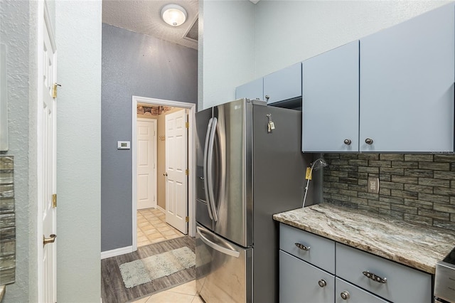 kitchen featuring light stone counters, a textured ceiling, stainless steel fridge, light tile patterned floors, and decorative backsplash