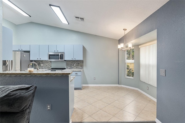 kitchen with kitchen peninsula, decorative backsplash, lofted ceiling, an inviting chandelier, and appliances with stainless steel finishes