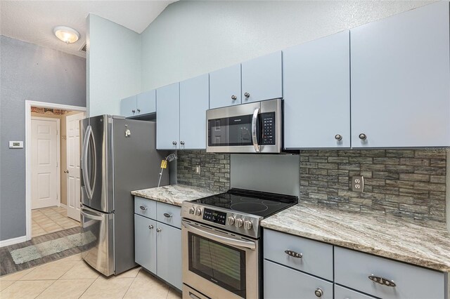 kitchen with light tile patterned floors, blue cabinetry, backsplash, light stone countertops, and appliances with stainless steel finishes