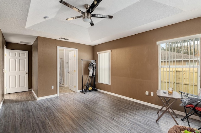 interior space featuring a raised ceiling, a textured ceiling, hardwood / wood-style floors, and ceiling fan