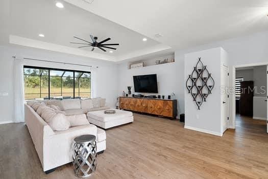 living room featuring ceiling fan, a raised ceiling, and wood-type flooring