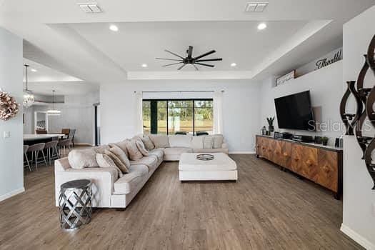 living room with a raised ceiling, ceiling fan, and dark wood-type flooring