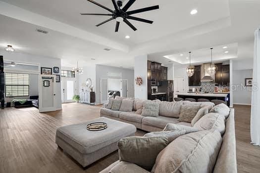 living room with a tray ceiling, light hardwood / wood-style floors, and ceiling fan with notable chandelier