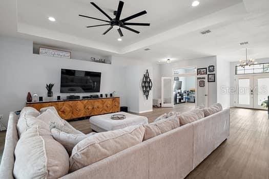 living room featuring a raised ceiling, french doors, ceiling fan with notable chandelier, and hardwood / wood-style flooring