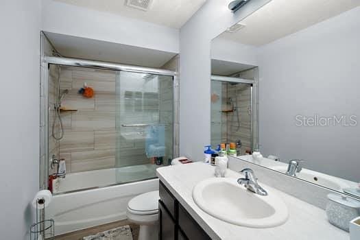 full bathroom with combined bath / shower with glass door, toilet, and vanity