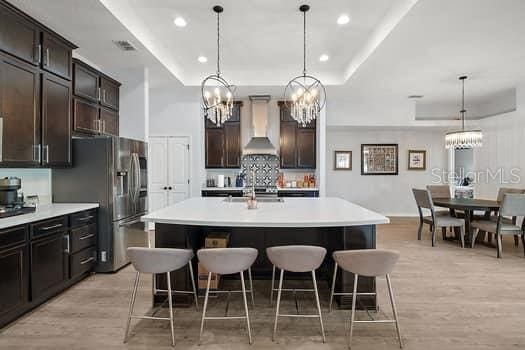 kitchen with a breakfast bar, an island with sink, decorative light fixtures, and wall chimney range hood