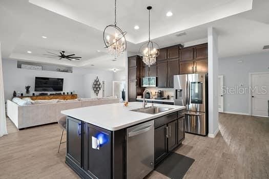 kitchen featuring stainless steel appliances, a raised ceiling, sink, a center island with sink, and light hardwood / wood-style flooring