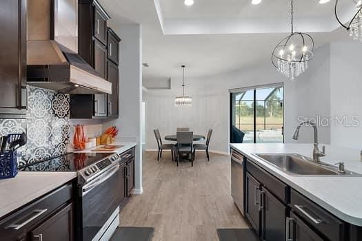 kitchen with decorative light fixtures, sink, wall chimney range hood, and stainless steel appliances