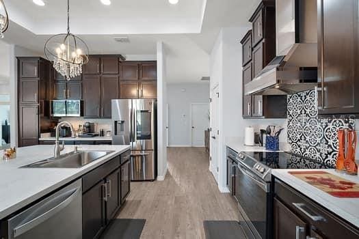 kitchen featuring sink, hanging light fixtures, stainless steel appliances, an inviting chandelier, and light wood-type flooring