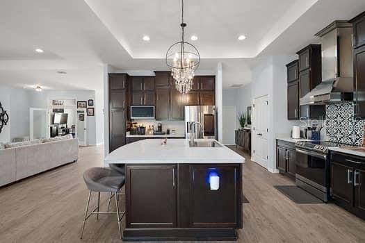 kitchen with appliances with stainless steel finishes, light wood-type flooring, wall chimney exhaust hood, sink, and an island with sink