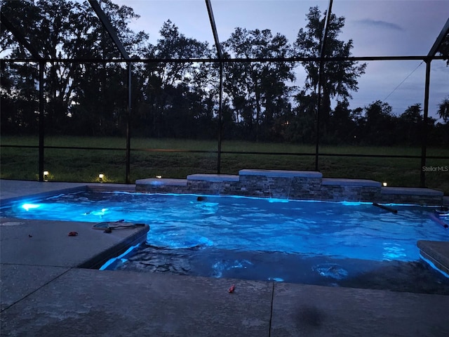 pool at dusk featuring pool water feature and glass enclosure