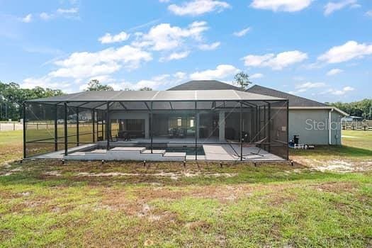 rear view of property with a lanai, a patio area, a lawn, and a pool