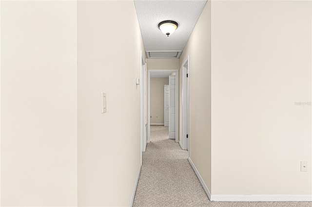 hallway with a textured ceiling and light carpet