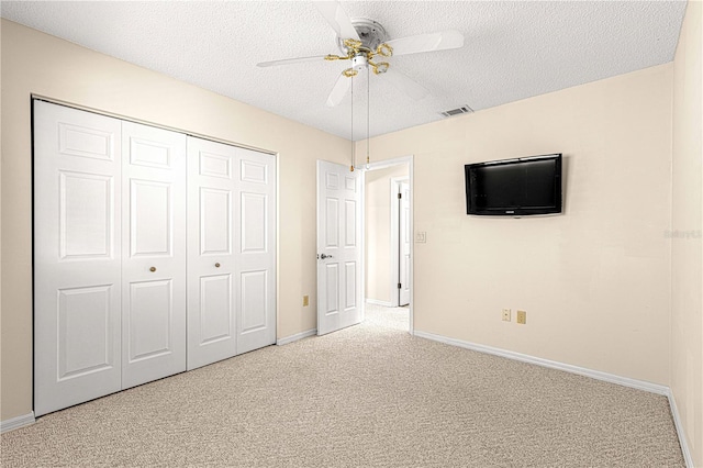 unfurnished bedroom featuring ceiling fan, a closet, light carpet, and a textured ceiling