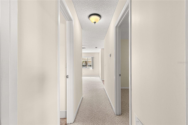 corridor with light colored carpet and a textured ceiling