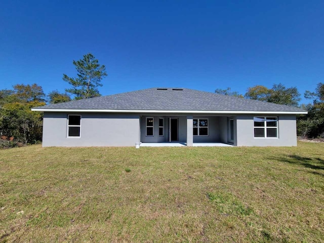 rear view of property with a shingled roof, a patio, a lawn, and stucco siding