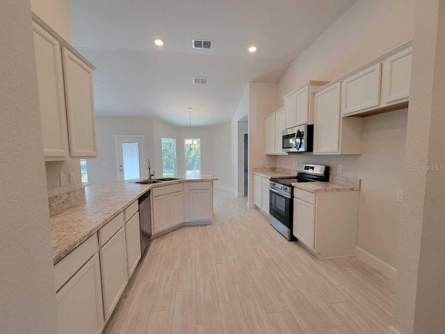 kitchen featuring light wood finished floors, visible vents, appliances with stainless steel finishes, a peninsula, and a sink