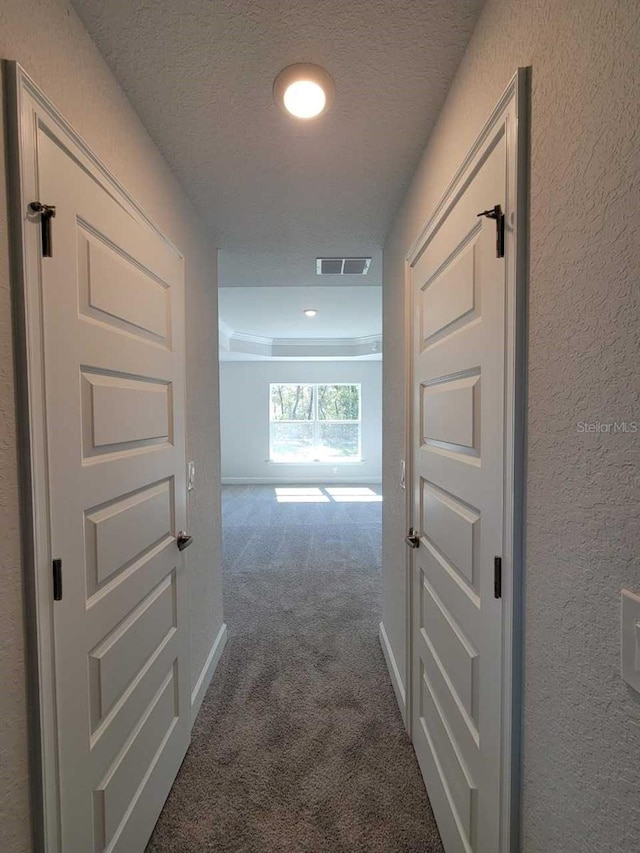 hallway with a textured wall, visible vents, dark carpet, and a textured ceiling