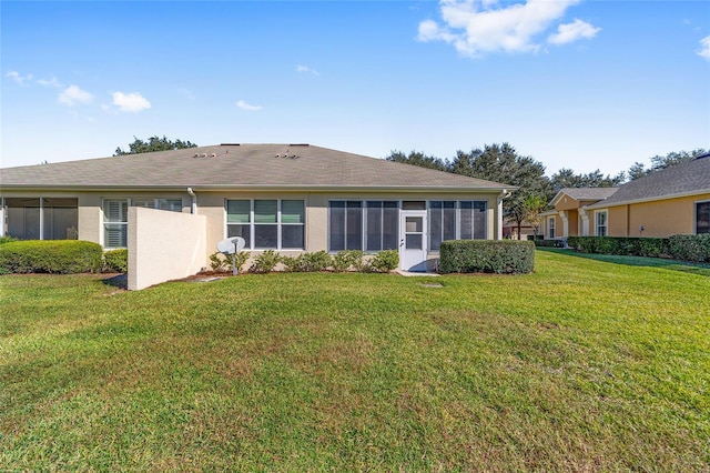 back of house featuring a sunroom, a lawn, and stucco siding