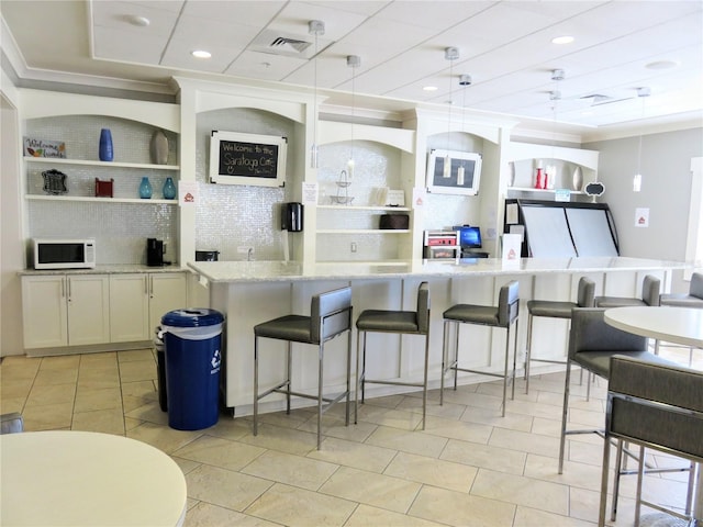 kitchen featuring white microwave, a breakfast bar, white cabinets, light stone countertops, and decorative light fixtures