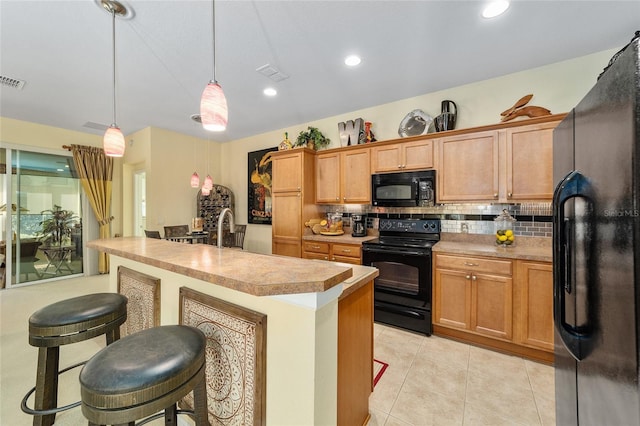 kitchen with decorative light fixtures, a center island with sink, visible vents, light countertops, and black appliances