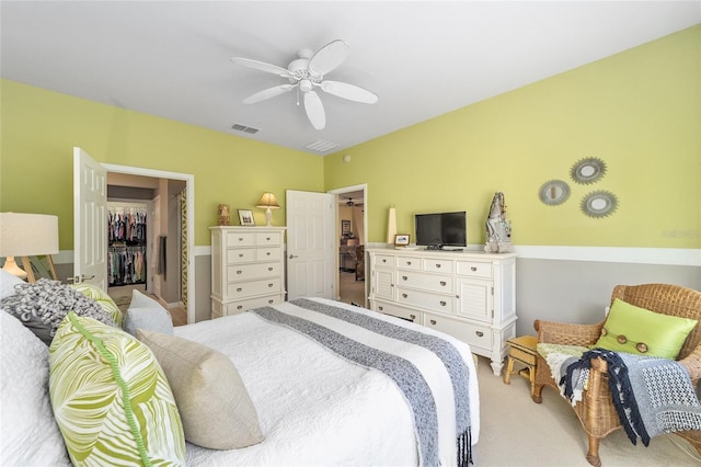 bedroom featuring a walk in closet, visible vents, ceiling fan, and light carpet