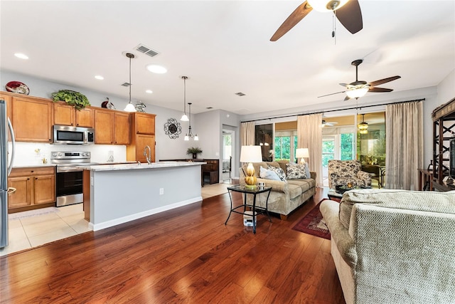 kitchen featuring hardwood / wood-style floors, sink, hanging light fixtures, an island with sink, and stainless steel appliances