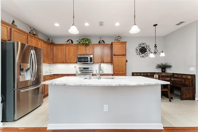 kitchen featuring light stone countertops, sink, decorative light fixtures, a kitchen island with sink, and appliances with stainless steel finishes